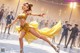 A woman in a yellow dress skating on a ice rink.