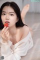 A woman laying on the floor eating a strawberry.