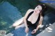 A woman in a black bathing suit sitting on the edge of a pool.