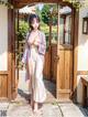 A woman in a kimono standing in front of a wooden door.